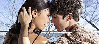A couple sits on a bench outside while embraced.