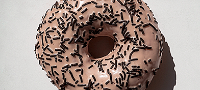 A pink donut with black sprinkles against a white background.