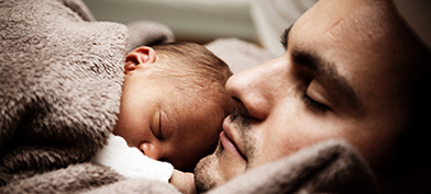 thumbA father holds his newborn baby on his chest while laying down.