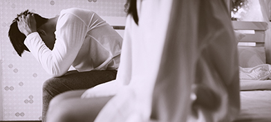 A couple sits on the side of a mattress in distress about erectile dysfunction.