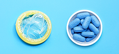Blue pills sit in a small open white container next to a condom on a blue surface.