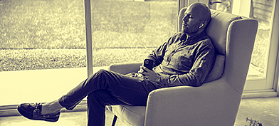 A man sits in a chair with earbuds in listening to something playing on his cellphone.