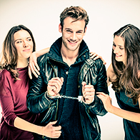 A man is smiling and handcuffed as he stands between two women.