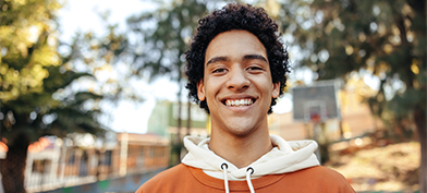 A-teenage-boy-stands-outside-and-smiles-at-the-camera
