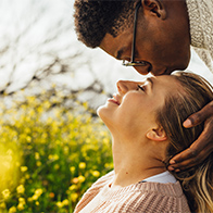 A man leans over a woman and kisses her forehead.