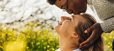 A man leans over a woman and kisses her forehead.