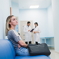 A woman sits on a hospital bench with two doctors in the background.