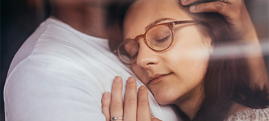A woman in glasses rest her cheek against her spouse's chest.