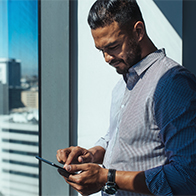 A man stands near a window reading his cellphone.
