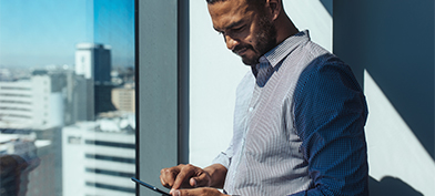 A man stands near a window reading his cellphone.