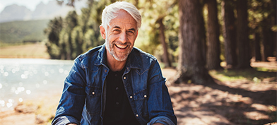 A-white-haired-man-sits-in-the-wood-smiling-at-the-camera