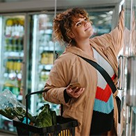 A woman is grocery shopping and reaching into the freezer.