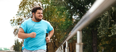 A man runs down the street, wearing blue and listening to music.