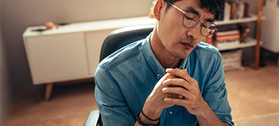 A man in glasses leans his head to the side with closed eyes and a distressed expression.