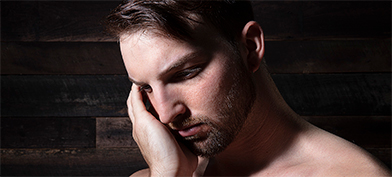 A man rubs his face while looking downward.