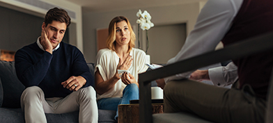 A man rubs his face while his partner talks to a licensed professional during couples therapy.