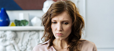 A woman going through divorce sits on a sofa staring downward.