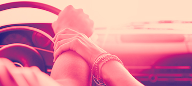 A man has hand on the steering wheel of a car while a woman lovingly holds his wrist.