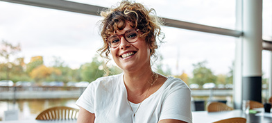 A woman sitting in a cafe smiles at the camera.