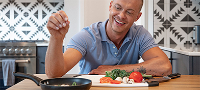 A man is putting a pinch of seasoning into a pan while cooking.