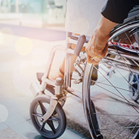 A person sits in a wheelchair and holds the frame with the sun shining down on them.