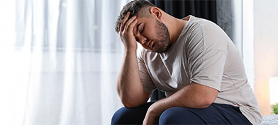 A sitting man has his elbow propped up on his knee and his head in his hand.