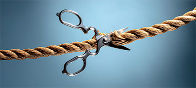 A pair of scissors is cutting a thick brown rope.