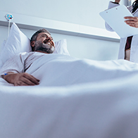 A man smiles in a hospital bed while looking up at his doctor after a vasectomy.