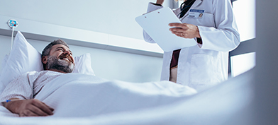 A man smiles in a hospital bed while looking up at his doctor after a vasectomy.