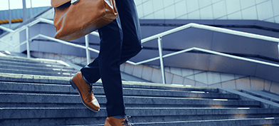 A person walks down the stairs outside while holding a briefcase.