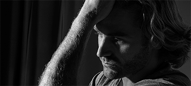 A close up of a man looking concerned while holding his head against his hand.