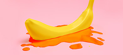 A banana sits in a small pool of blood on a pink background.