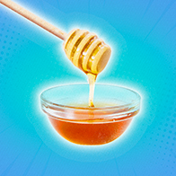 Honey is falling down from a dipper into a small dish against a blue background.