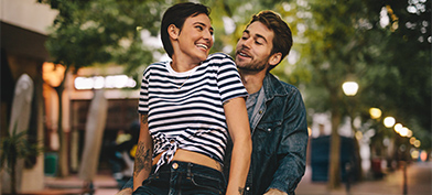 A woman sitting on bicycle handlebars smiles back at the man riding the bike.