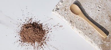 A wooden spoon on a stone plate lies next to a pile of brown powder.
