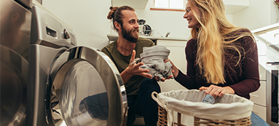 A woman hands her smiling partner laundry from the drying machine.