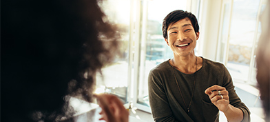 A man smiles at his friends in the kitchen as he brings food to his mouth. 