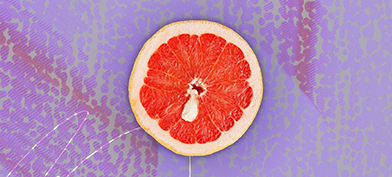 Half of a grapefruit is against a purple background and has a white cyst towards the middle of it.