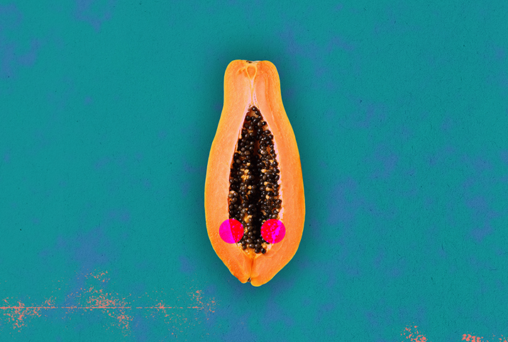 Half of a papaya is against a teal background with two red dots along either side of the open center.