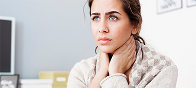 A woman rests her hands on her neck and looks concerned.