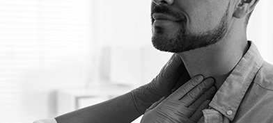 Two gloved hands palpate a bearded man's neck.