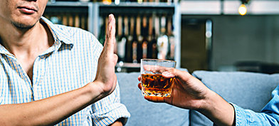 A man holds his hand up to refuse an alcoholic drink being offered to him.