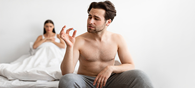 A man sitting on a bed holds up a prescription drug that could cause a low sex drive.