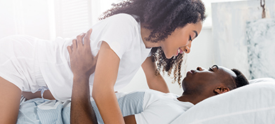 A couple are in bed with a woman on top smiling down at a man.