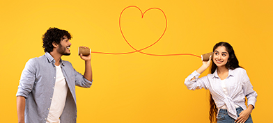 A man talks into a cup with a string in the shape of a heart leading to another cup that has a woman listening.