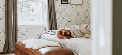 The feet of a couple shows from under the blankets while they lie in bed together.