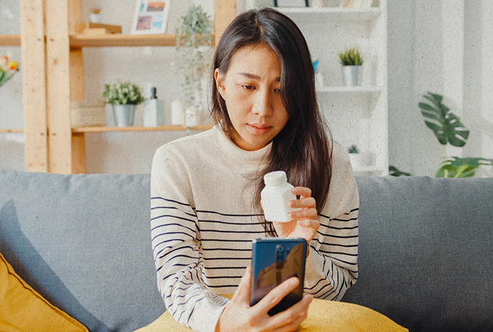 A woman holds up a medicine bottle to her phone on a video call with her telehealth provider.