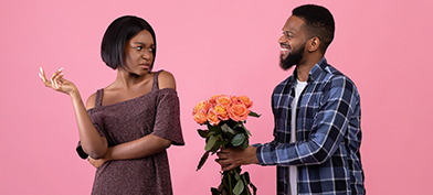 A man tries to give flowers to a woman while she is scowling at him.
