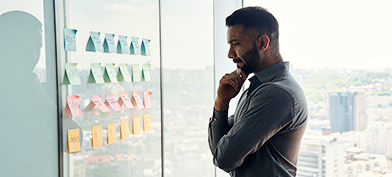 A man stares at a collection of post-it notes placed on a wall at work.