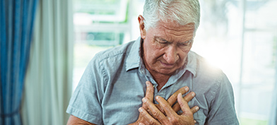 An elderly man with white hair clutches his chest and looks downward.